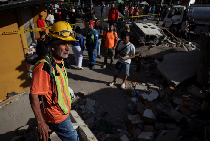 People gather as emergency personnel work at the site of a damaged building
