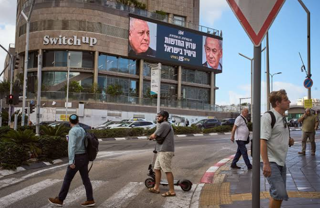 People walk past a television channel advertisement featuring Israeli Prime Minister Benjamin Netanyahu, right, and his main rival